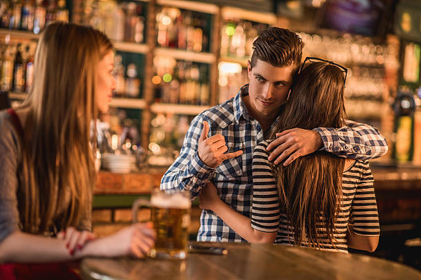 Man hugs his girlfriend while looking at a different girl, making a "call me" gesture with his hand