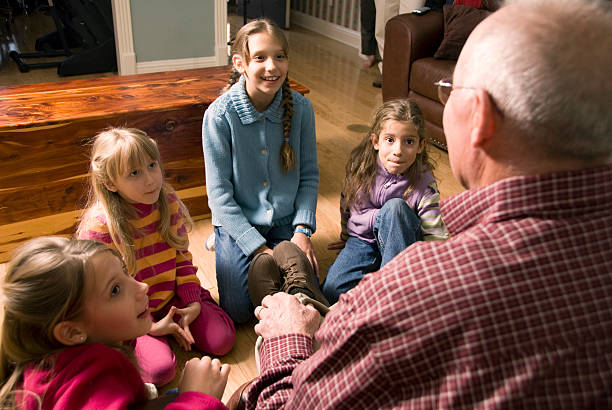 Grandfather tells a story to his granddaughters who are seated on the floor around him