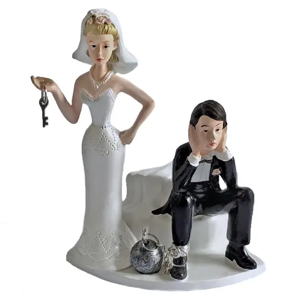 Wedding cake topper depicting a sad groom with a ball and chain around his ankle, and a bride smugly holding a key