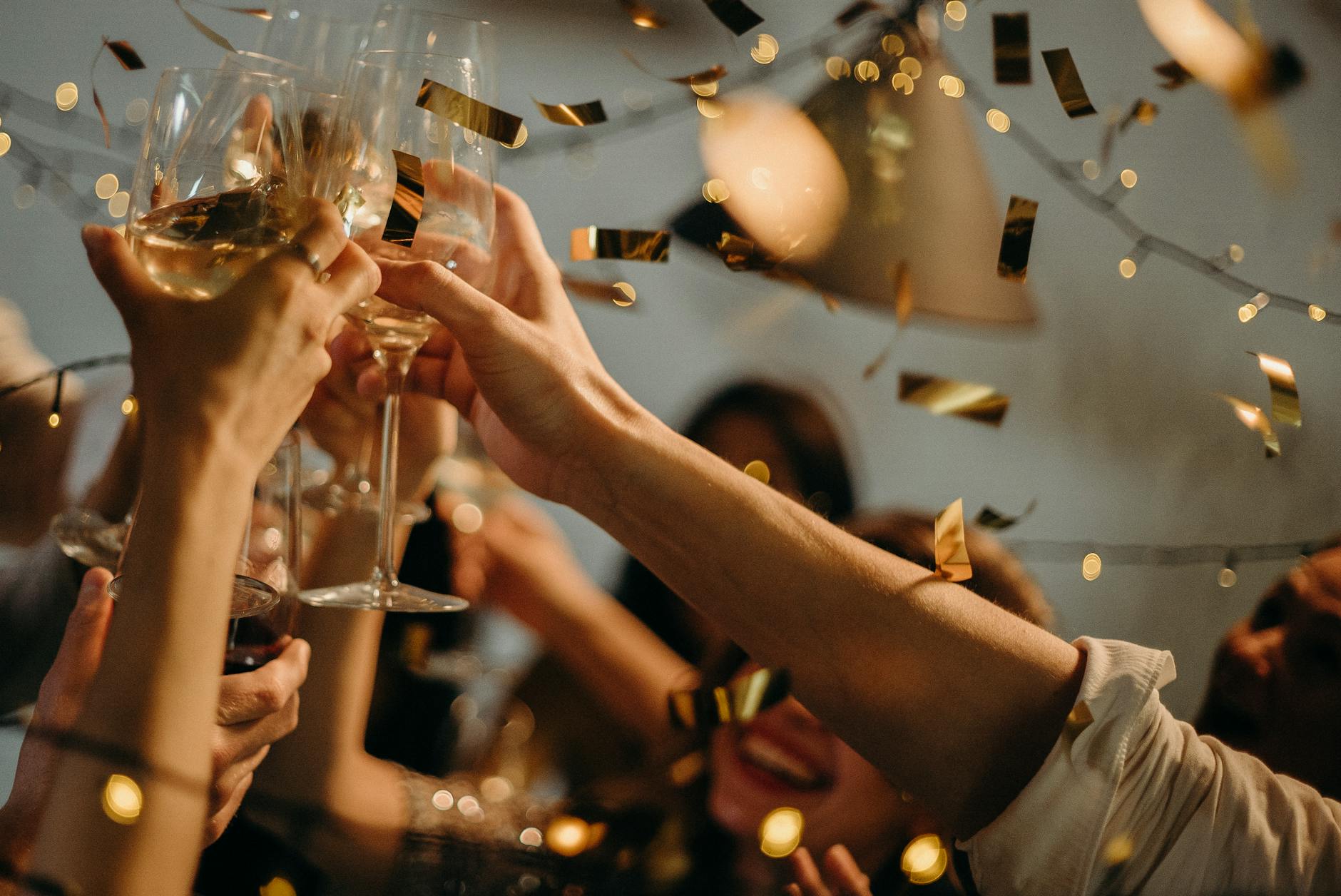 A group of people toasting with champagne glasses, surrounded by festive confetti and warm, glowing lights, celebrating together.